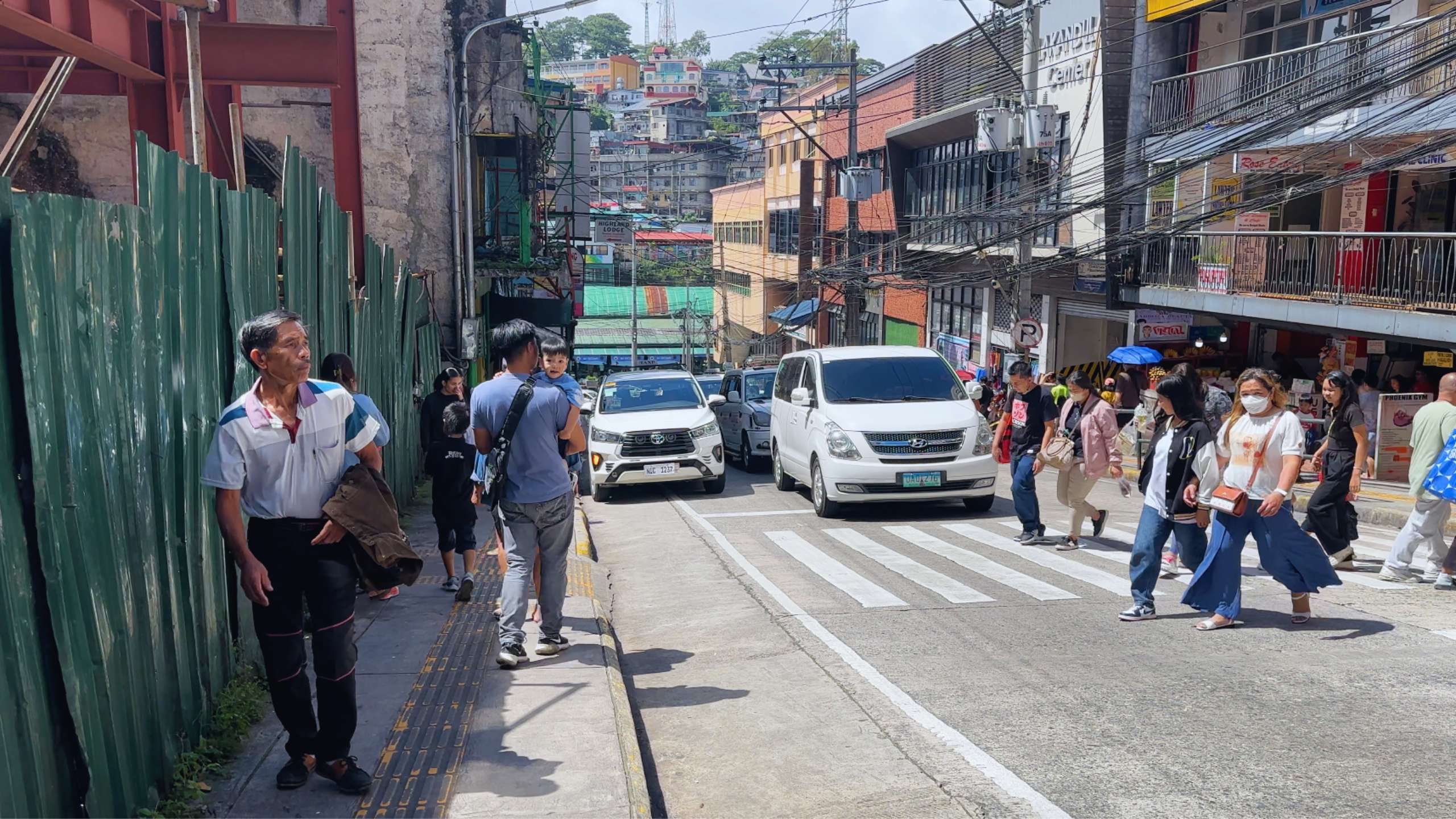 People walk through a vibrant street with a view of the hillside buildings.