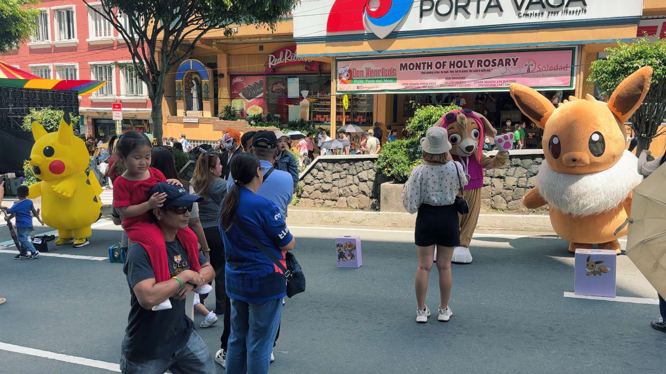 Children interact with giant mascot characters in a festive street scene.