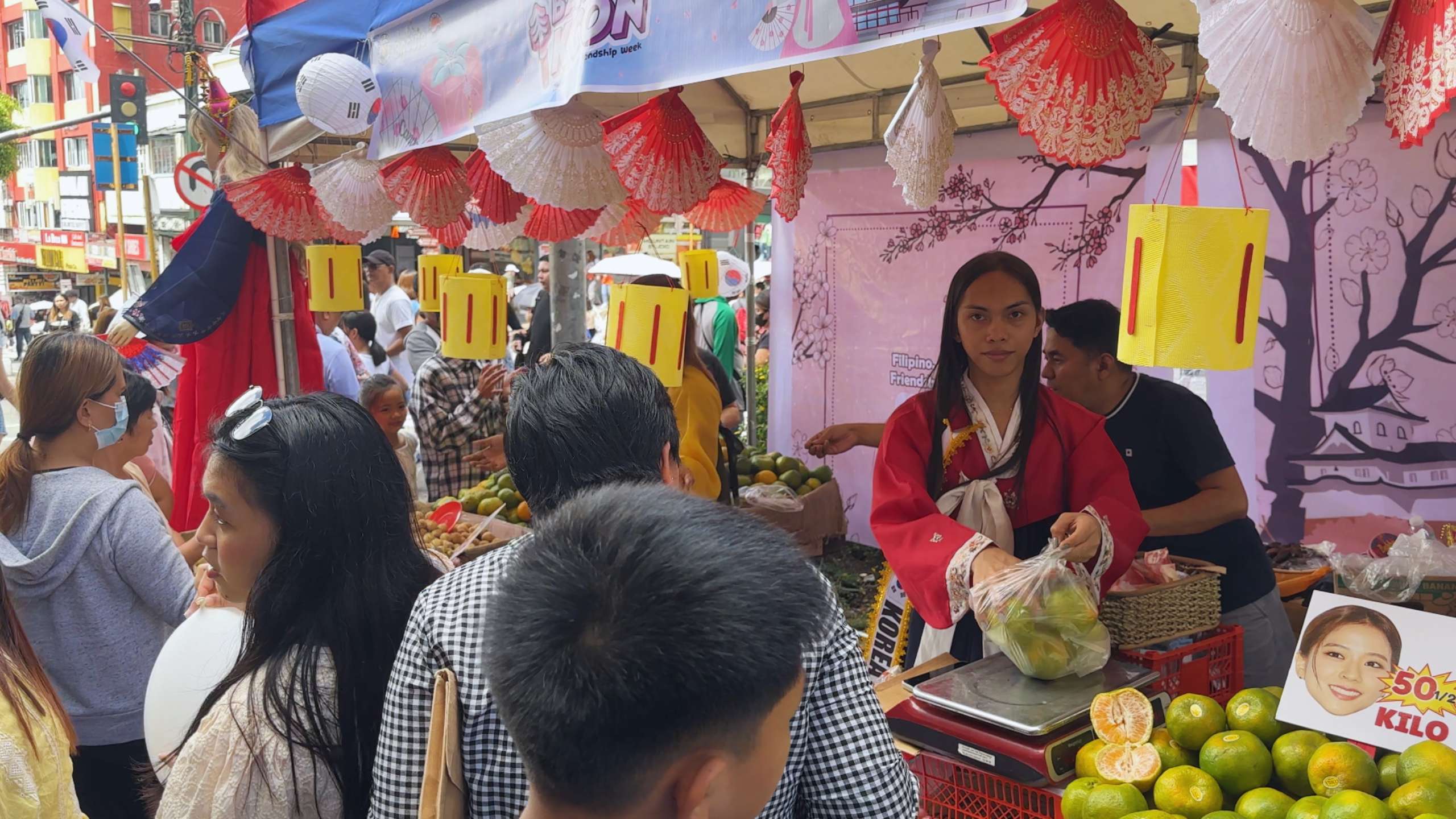 A traditional stall sells fresh fruit with colorful fans and lanterns as decoration.