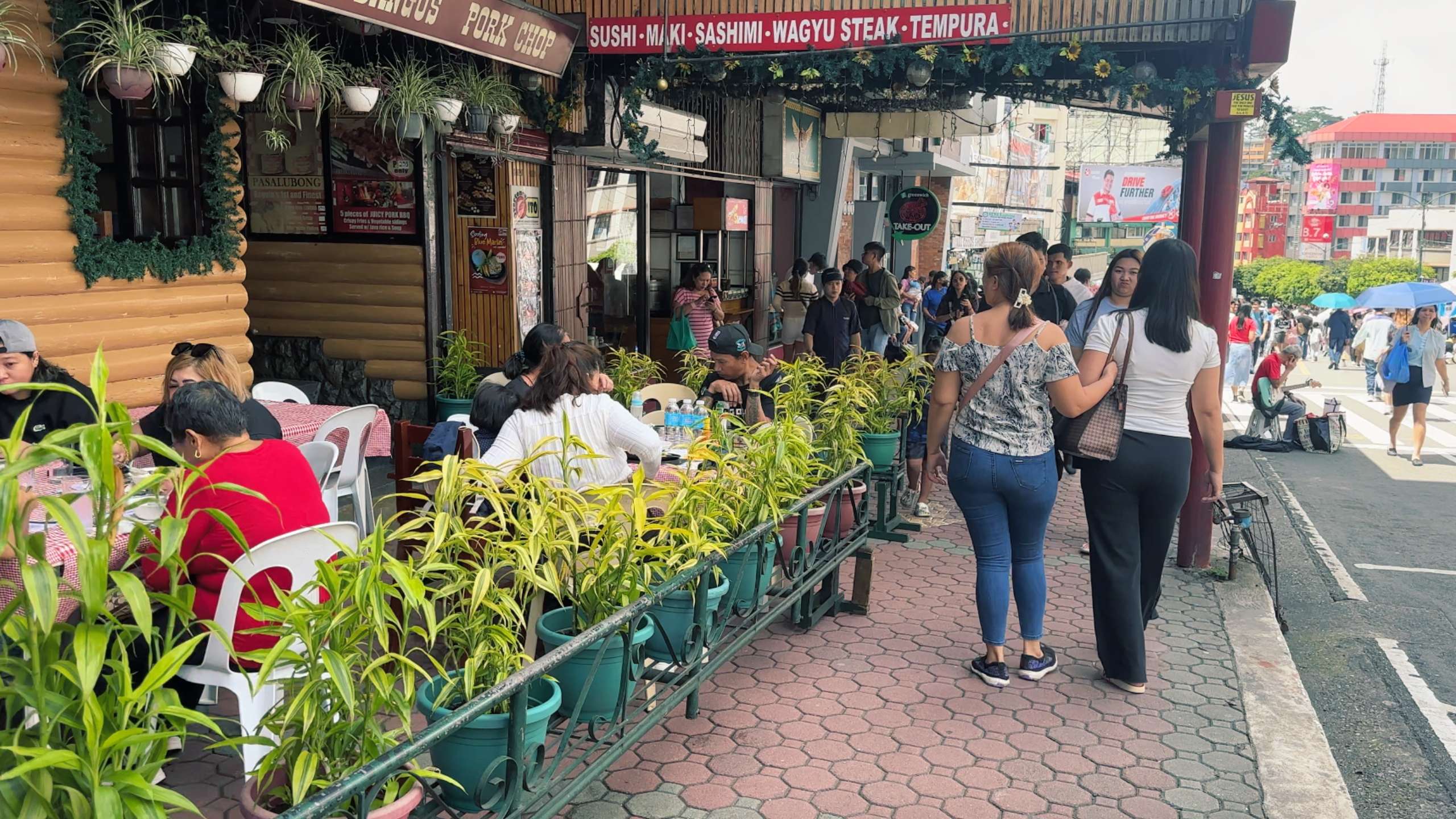 A cozy cafe with hanging plants and tables draws in people for food and drinks.